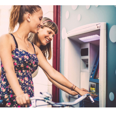 Photo of two teenage girls using an ATM one girl is riding a bicycle
